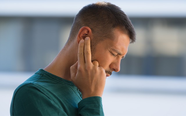 Mann mit Tinnitus hält sich das Ohr fest